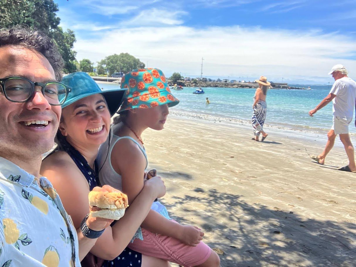 Eliza, Sam, and Annie Grove on a New Zealand beach, a close family selfie with the sea behind them